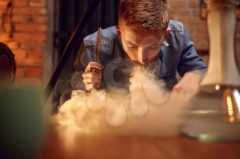 Young man blows smoke on the table in hookah bar, hooka. Shisha smoking, traditional bong culture, tobacco aroma for relaxation, rest with hooka
