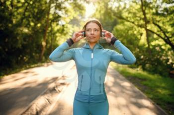 Morning training in park, woman in headphones listens to music on walkway. Female runner goes in for sports at sunny day, healthy lifestyle, jogger on outdoors workout