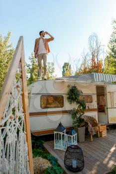 Man standing on rv roof, trailer camping. Couple travels on van, romantic vacations on motorhome, camper leisures in camping-car, camp in forest