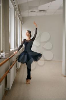 Ballerina doing exercise at barre in class. Ballet training, dance studio interior on background, elegant female dancer, beautiful grace