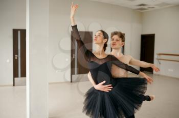 Female and male ballet dancers in action. Ballerina with partner training in class, dance studio interior on background
