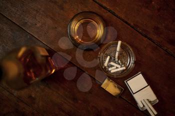 Cigarette in ashtray and alcohol beverage in bottle on wooden table, top view, nobody. Tobacco smoking culture, specific flavor. Bad habits concept