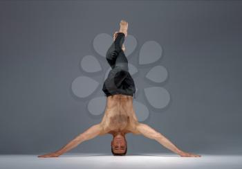 Male yoga standing on his head and hands, meditation, grey background. Strong man doing yogi exercise, asana training, top concentration, healthy lifestyle