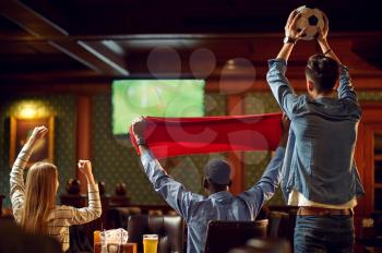 Happy football fans with red scarf and ball watching game tv broadcasting, friends in bar. Group of people relax in pub, night lifestyle, friendship, sport victory celebration