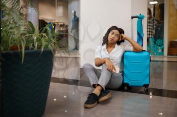 Tired woman with suitcase sitting on the floor in airport. Female person with luggage, international air gate, passenger with bag. Girl with baggage in departure terminal