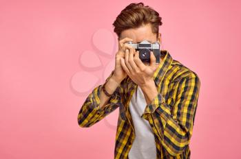 Portrait of young photographer with a camera, pink background. Face expression, male person poses in studio, genre concept, occupation