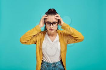 Stressed woman in glasses, blue background, negative emotion. Face expression, female person looking on camera in studio, emotional concept, feelings