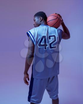 Basketball player poses with ball in studio, back view, neon background. Professional male baller in sportswear playing sport game, tall sportsman