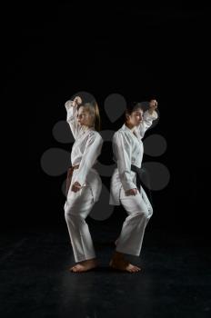 Female karatekas in white kimono, combat stance in action, dark background. Karate fighters on workout, martial arts, women fighting