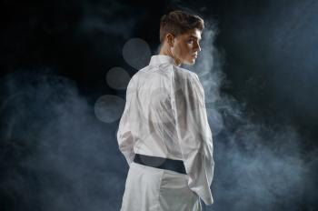 Male karateka, fighter having black belt, back view, dark background. Man on karate workout, martial arts, training before fighting competition