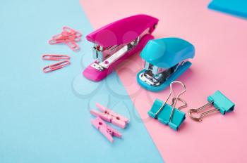 Stapler and paper clips closeup, blue and pink background. Office stationery supplies, school or education accessories, writing and drawing tools