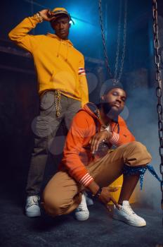 Two stylish rappers poses in studio with cool underground decoration. Hip-hop performers, trendy rap singers, break-dancers