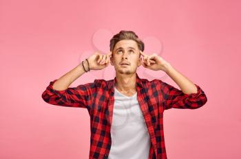 Focused man with a finger at his temple, pink background, emotion. Face expression, male person looking on camera in studio, emotional concept, feelings
