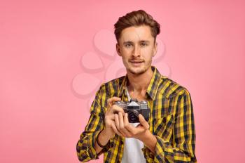 Portrait of young photographer with a camera, pink background. Face expression, male person poses in studio, genre concept, occupation