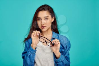 Attractive mysterious woman holds glasses, blue background, positive emotion. Face expression, female person looking on camera in studio, emotional concept, feelings