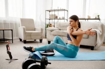 Smiling girl sits on the floor at home, online fitness training at the laptop. Female person in sportswear, internet sport workout, room interior on background