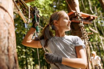 Little girl leisures in rope park, playground. Child climbing on suspension bridge, extreme sport adventure on vacations, danger entertainment outdoors