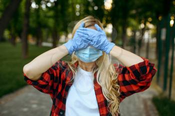 Young woman in mask and gloves covers her face in park, quarantine. Female person walking during the epidemic, health care and protection, pandemic lifestyle