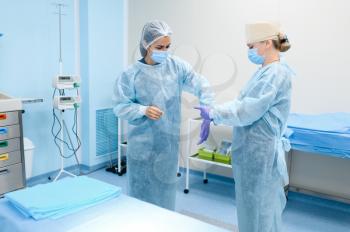 Female surgeon and assistant puts on a gloves in operating room, preparing for surgery operation. Doctor in uniform, medical clinic worker, medicine and health, healthcare in hospital
