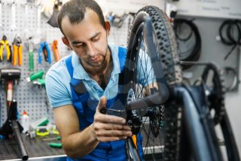 Bicycle assembly in workshop, chain installation. Mechanic in uniform fix problems with cycle, professional bike repairing service