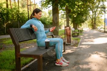 Woman in headphones relax on bench after morning workout in park. Female runner goes in for sports at sunny day, healthy lifestyle, sportive girl on outdoors training