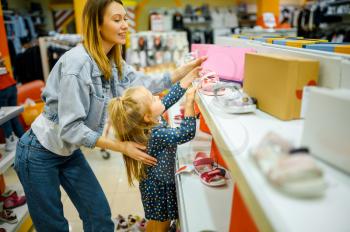 Mother and little baby looking on shoes in kid's store. Mom and adorable girl near the showcase in children's shop, happy childhood, family makes a purchase in market