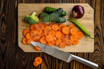 Fresh cutted vegetables on board and knife isolated on wooden background. Organic vegetarian food, grocery assortment, natural eco products, healthy lifestyle concept