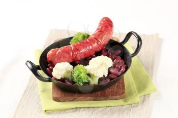 Sausage, beans and vegetables on a black pan 