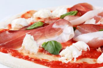 Raw pizza dough with mozzarella and proscuitto on top