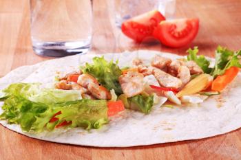 Grilled chicken strips and fresh vegetables spread on tortilla