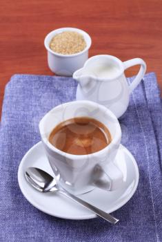 Cup of coffee, jug of milk and brown sugar