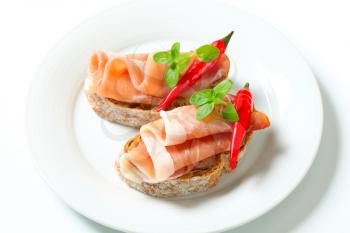 Prosciutto open faced sandwiches garnished with red chili peppers