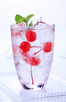 Glass of iced drink with maraschino cherries