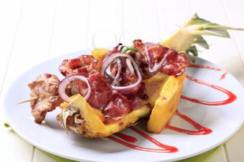 Meat skewers and pan fried bacon strips on pineapple