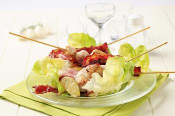 Chicken skewers and bacon strips served on lettuce leaves