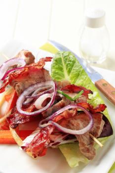 Grilled meat on skewer with crispy rashers of bacon and vegetables