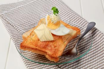 Two pieces of crispy toast, butter and boiled egg 