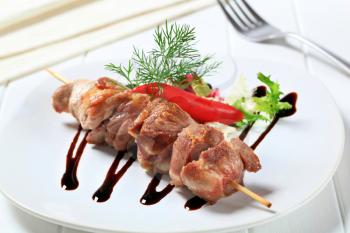 Pork skewer garnished with fresh salad and drizzle sauce