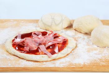 Raw pizza dough topped with ham 