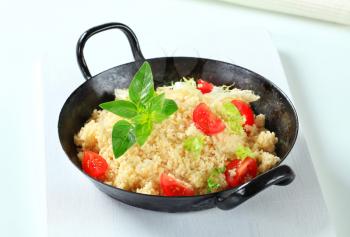 Couscous with salad greens and tomato in a pan