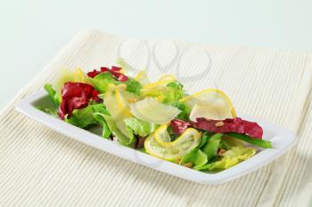Green salad with slices of lemon, Parmesan shavings and pine nuts