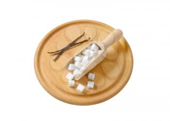 White sugar cubes in wooden scoop and vanilla pods