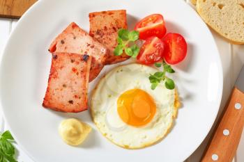 Pan-fried meatloaf with sunny side up fried egg and mustard