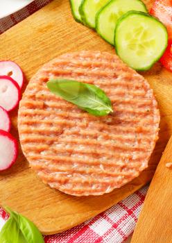 Raw burger patty and sliced vegetables on cutting board