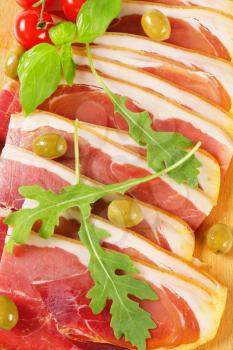 Sliced prosciutto crudo and green olives on cutting board