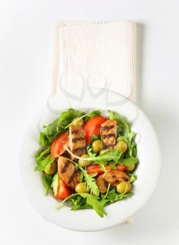 Sliced grilled patty on nest of rocket salad with tomato and olives