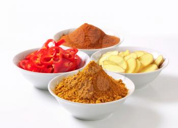 Bowls of curry powder, ground cinnamon, sliced ginger root and red pepper
