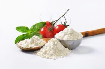 Pile of soft wheat flour, wooden spoon and fresh tomatoes