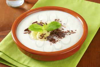 Bowl of smooth milk pudding with sliced banana and grated chocolate