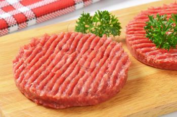 detail of two raw hamburger patties with parsley on wooden cutting board